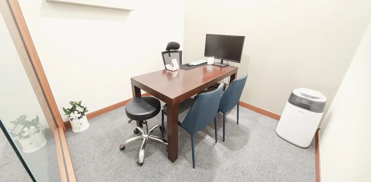 Small consultation room with a wooden desk, monitor and two chairs