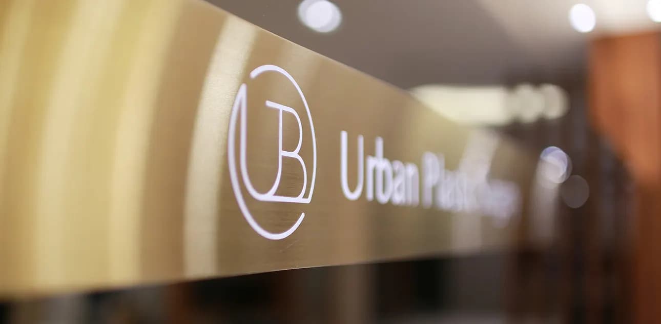 Gold-colored sign with the Urban Plastic Surgery logo