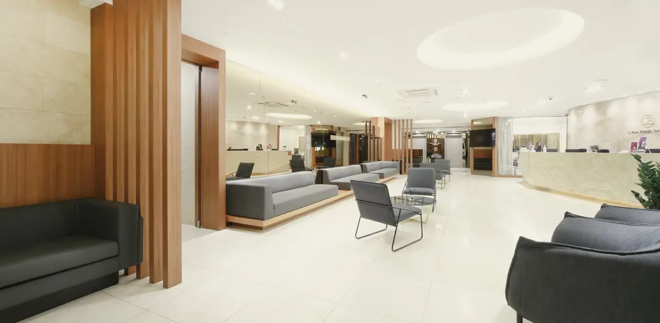 Waiting area with grey sofas and armchairs along a long, light-filled hall