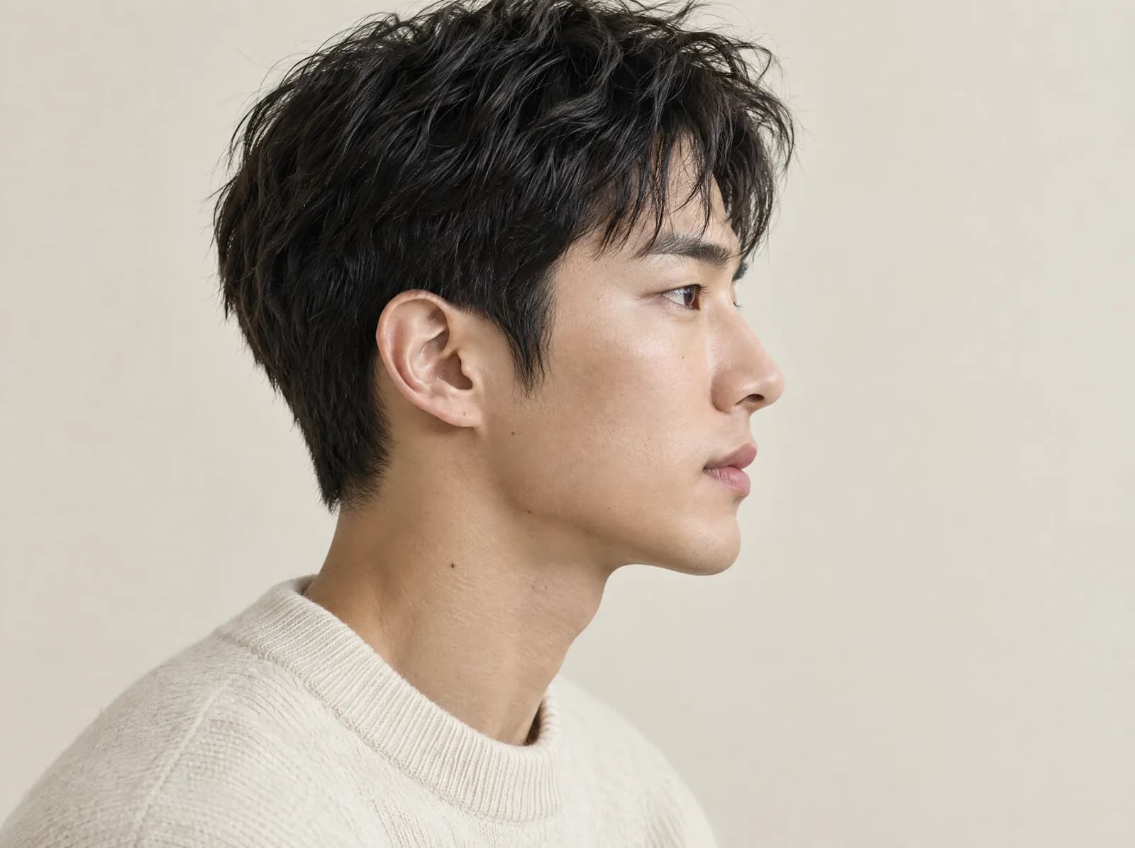ใบหน้าด้านข้างของชายหนุ่มชาวเกาหลีผมสั้นมีลอน สวมเสื้อไหมพรมสีครีม