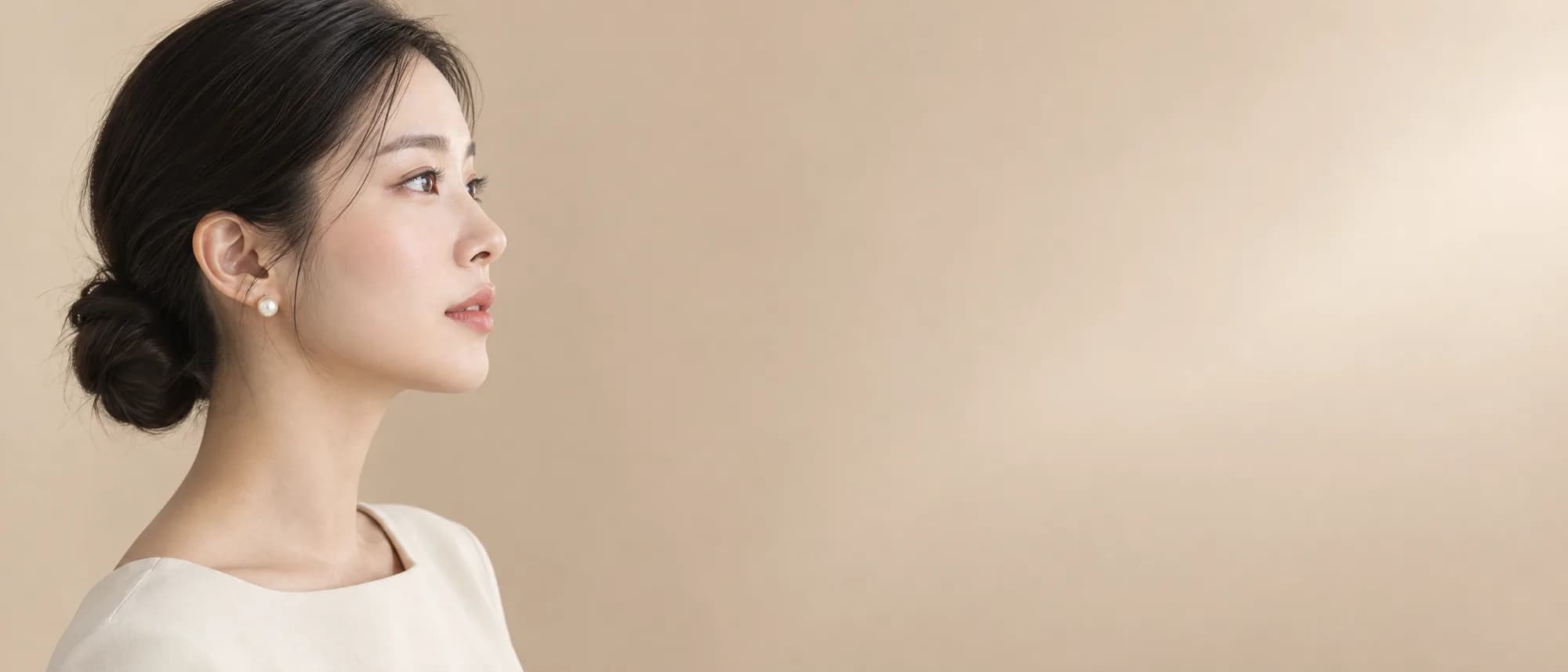 Một phụ nữ Hàn Quốc nhìn nghiêng, đeo bông tai ngọc trai, trước nền màu be ấm.