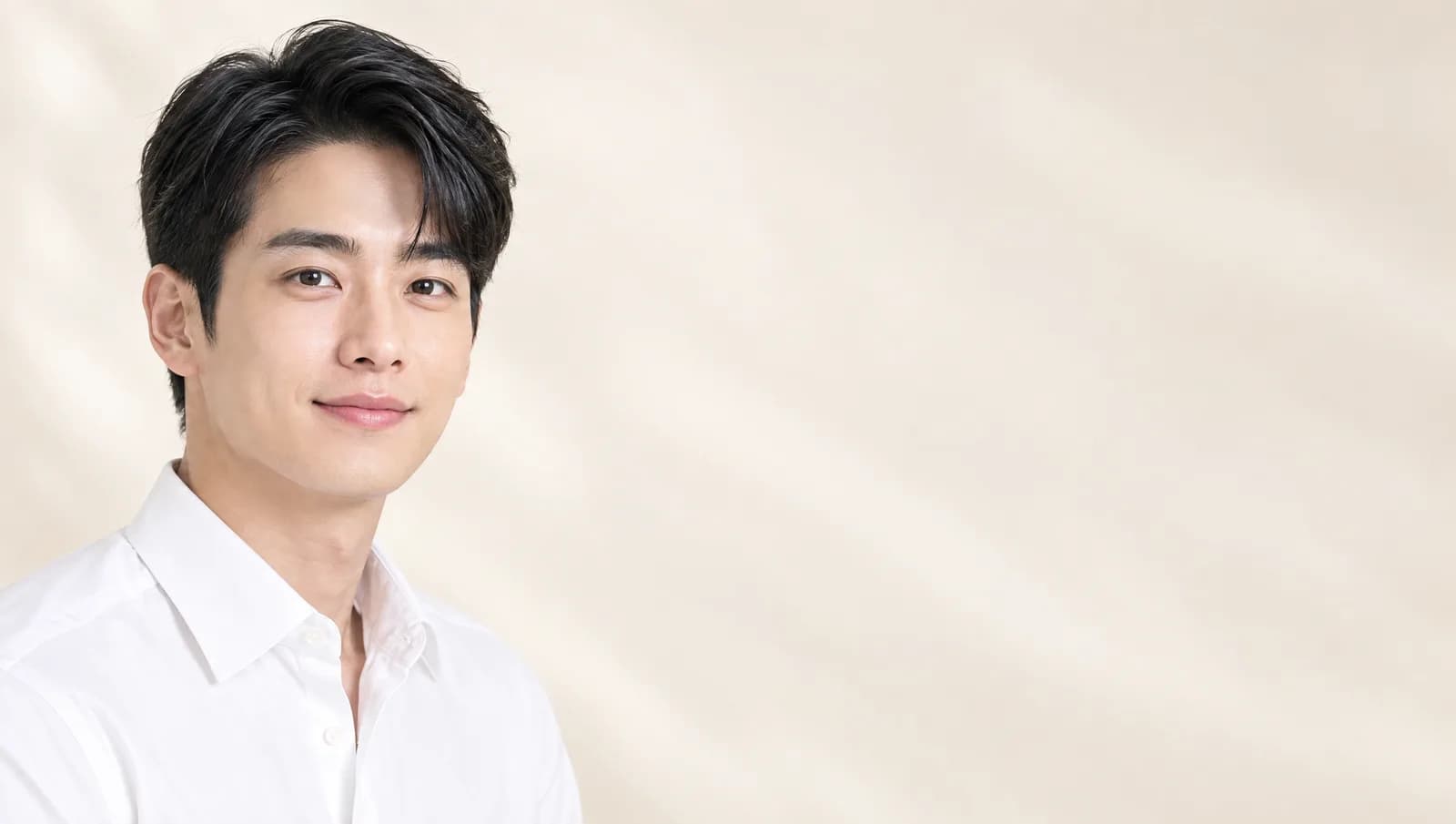 Một người đàn ông Hàn Quốc đang mỉm cười, mặc áo sơ mi trắng, ở phía bên trái của một tấm ảnh studio rộng, bên phải là ánh sáng màu kem dịu.