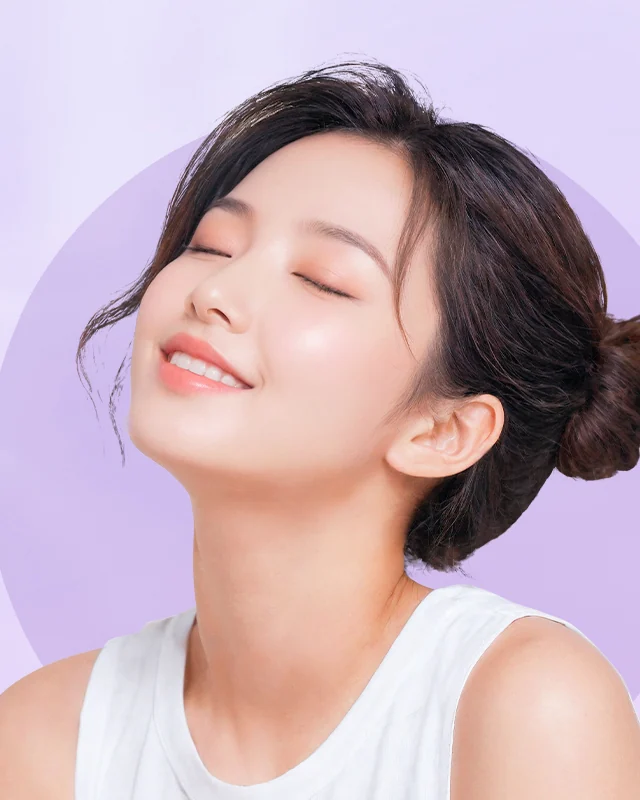 Seorang perempuan muda dengan rambut diikat ke belakang, mata terpejam dan wajah menengadah ke arah cahaya, dengan latar ungu muda yang lembut.